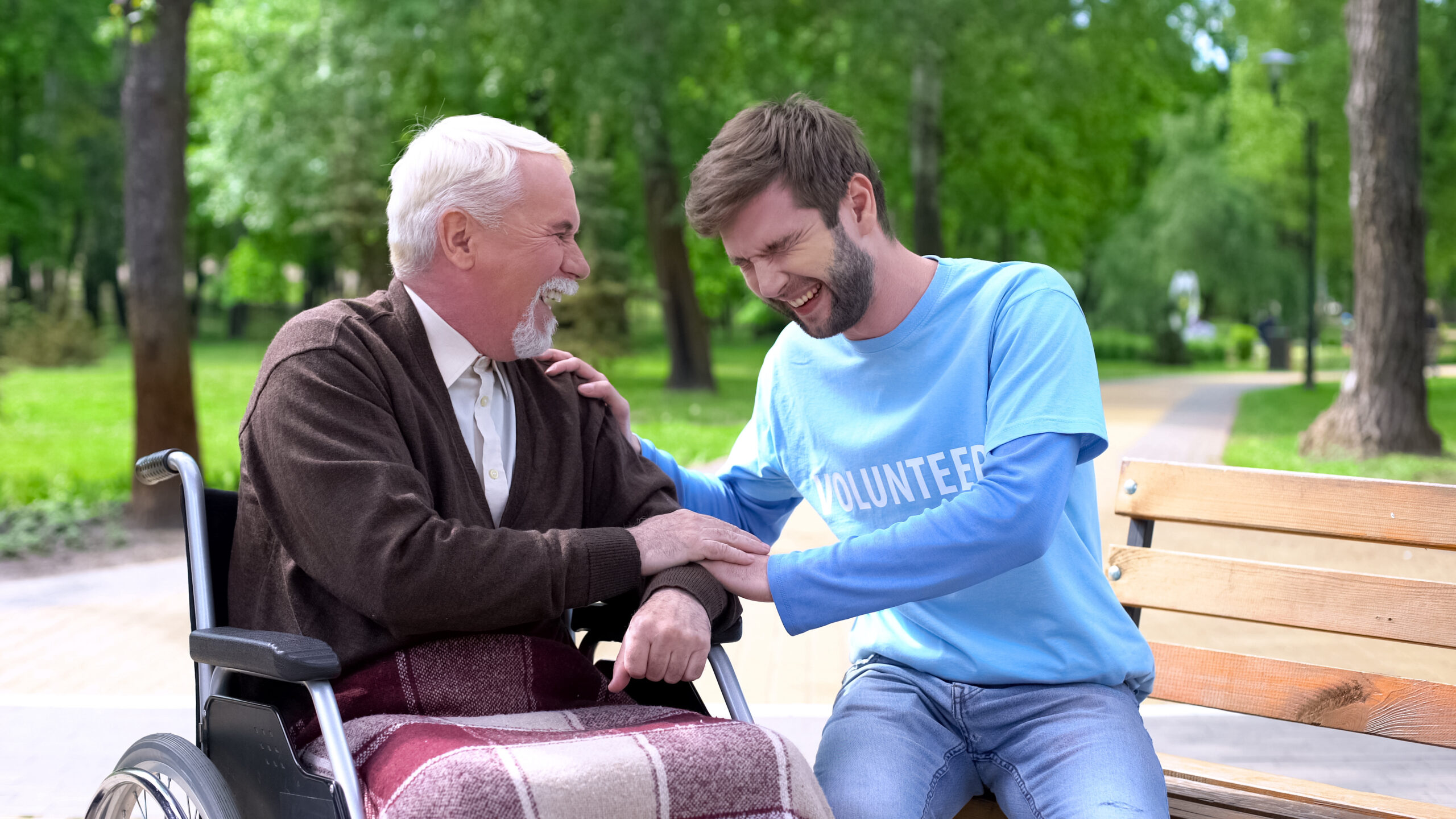 Aged male in wheelchair and hospice volunteer laughing and joking, having fun together