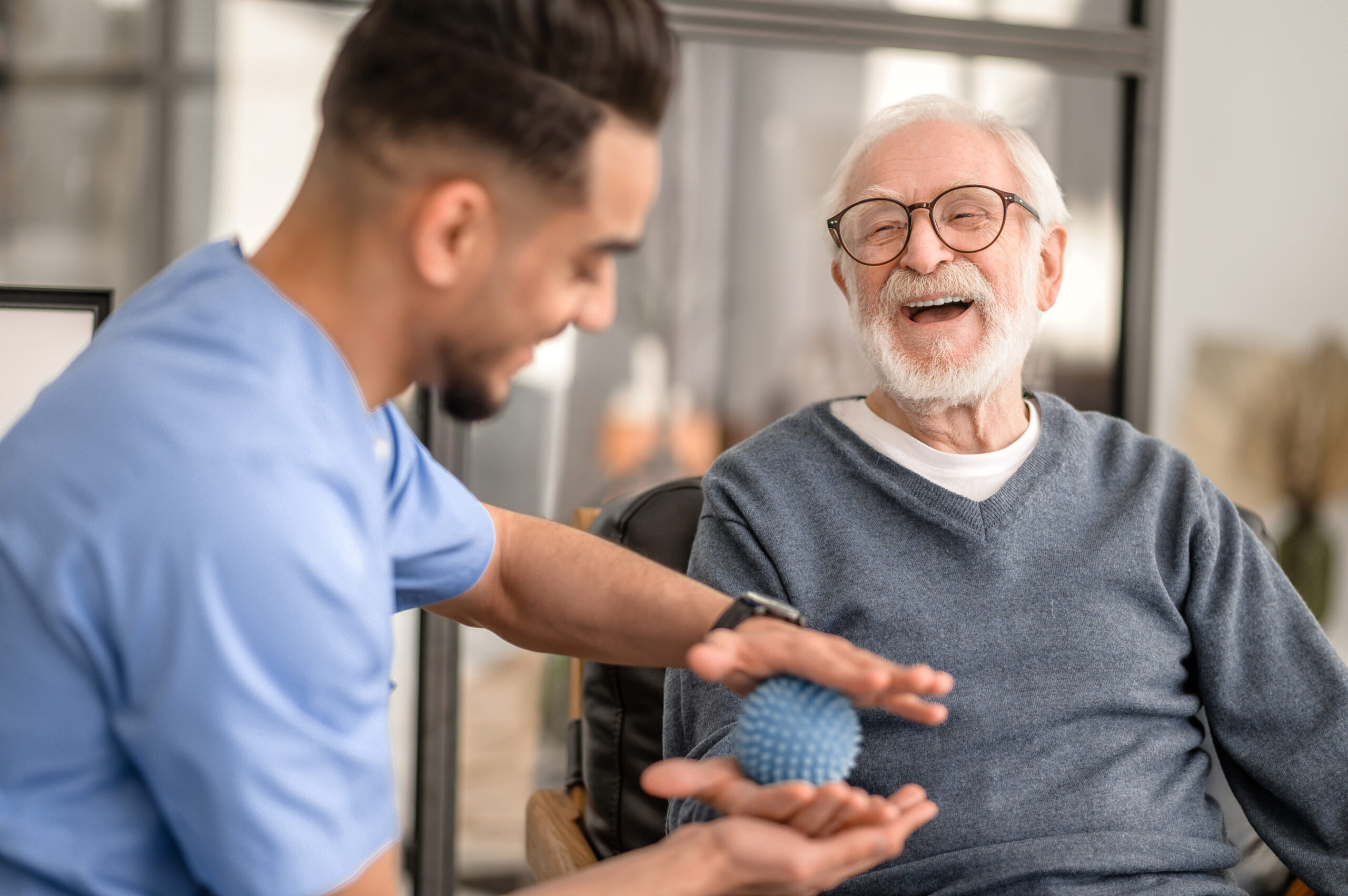 Joyous aged man undergoing a session of physical therapy conducted by an experienced physical therapist