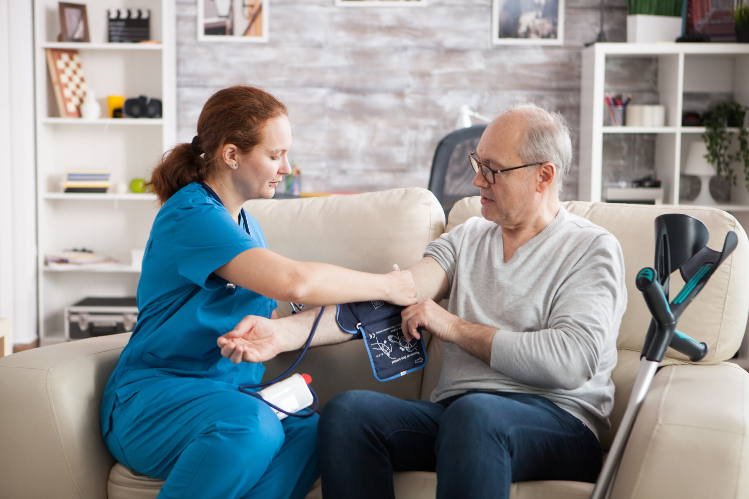 Young female nurse taking digital blood pressure of old man in his home.