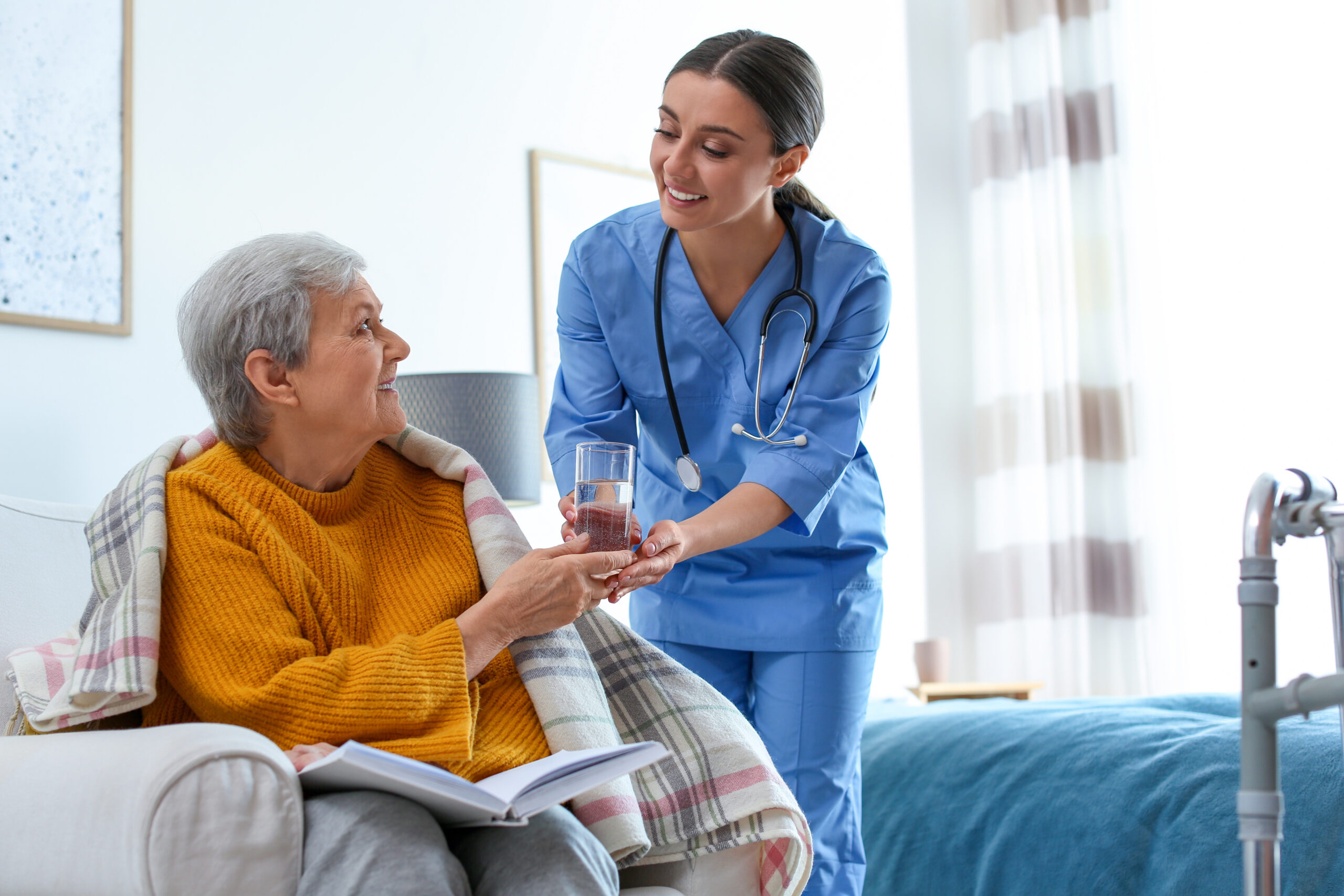 Hospice nurse giving water to an elderly woman in hospice care.