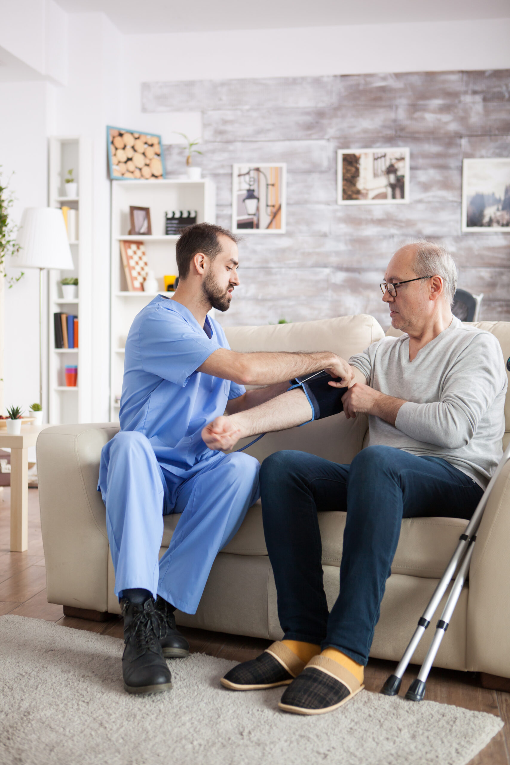 Young male nurse taking blood pressure of elderly age man at home.