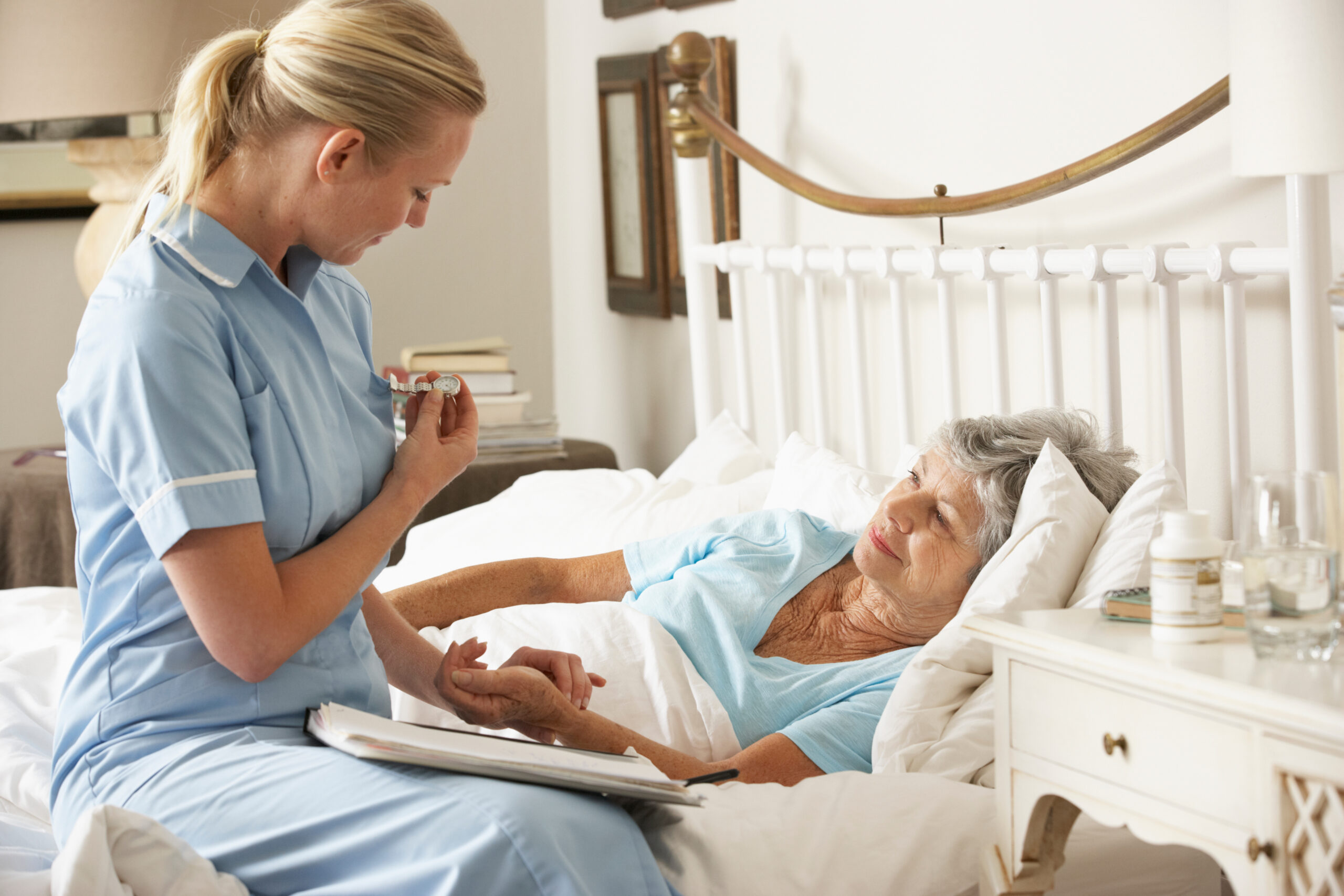 Female nurse checking the pulse of elderly woman lying in bed